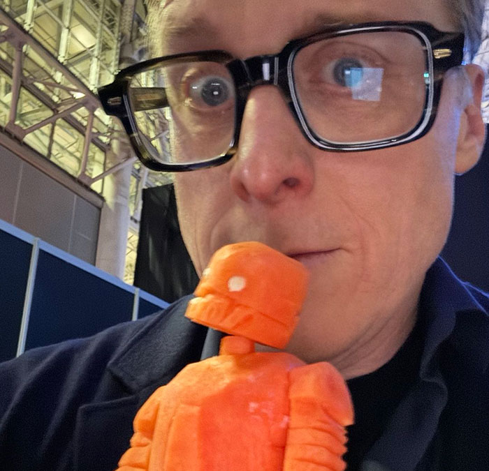 Co-actor wearing glasses holding an orange figurine, related to studio removing his name from publicity claims. Co-actor wearing glasses holding an orange figurine, related to studio removing his name from publicity claims.