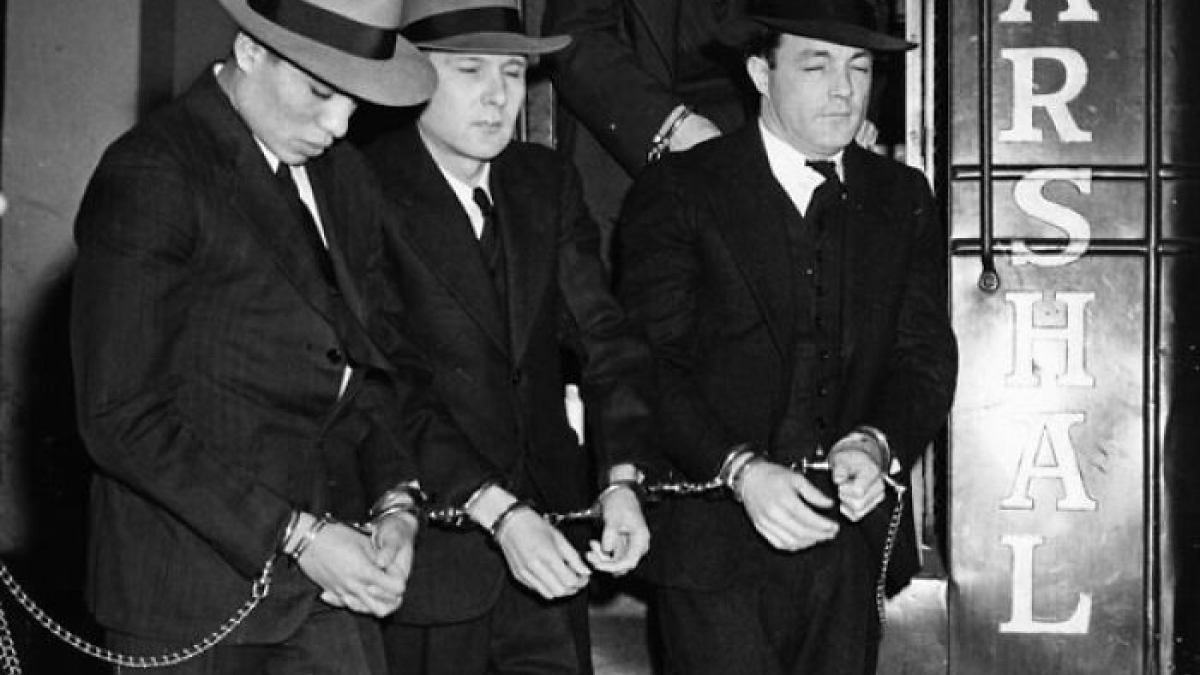 Three men in suits and hats, handcuffed and chained, depicting harsh reality of life on Alcatraz prison.