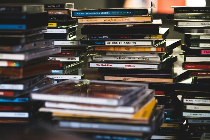 Stacks of CDs and cases in a dimly lit room, evoking unexpected and gross discoveries in strangers’ homes.