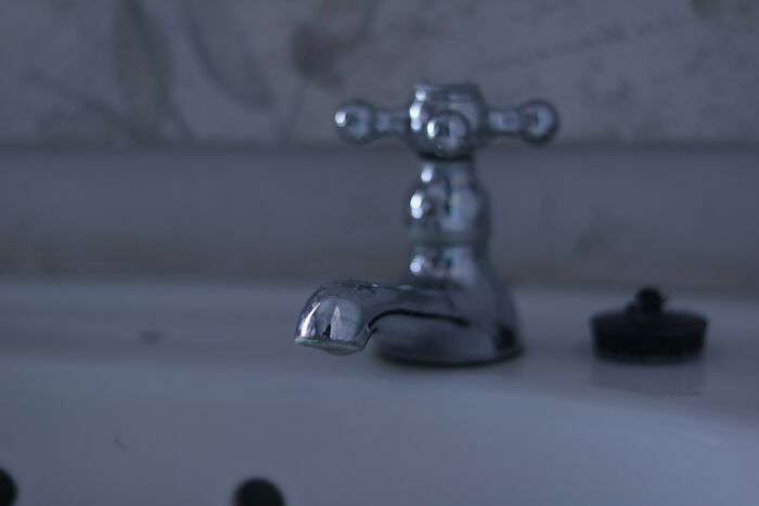 Close-up of an old, grimy faucet in a dimly lit bathroom reflecting the grossest, unexpected things in strangers’ homes.