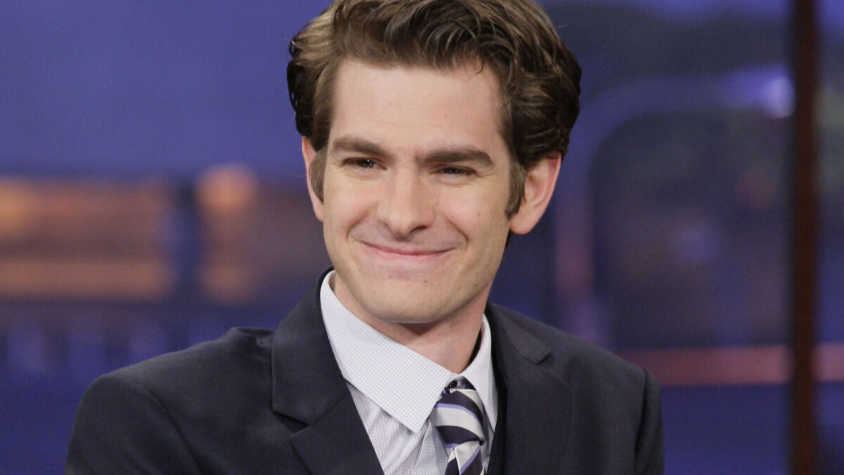 Andrew Garfield smiling in a dark suit and striped tie, sparking major botox buzz with his latest vampire look.