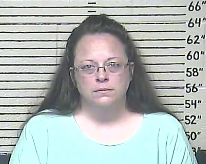 Mugshot of anti-LGBTQ activist Kim Davis against height chart wearing glasses and a light blue shirt. Mugshot of anti-LGBTQ activist Kim Davis against height chart wearing glasses and a light blue shirt.