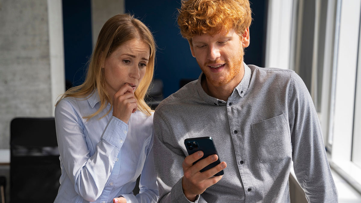 Young woman looking concerned as creepy guy incessantly texts her on phone in an office setting with natural light.