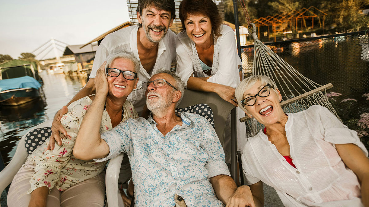 Group of mature adults laughing outdoors by water, highlighting gender-based double standards in social interactions.