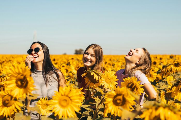 Three women smiling and laughing among sunflowers, highlighting themes of gender-based double standards and joy.