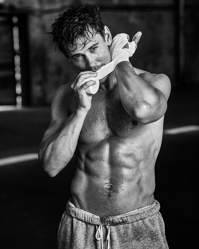 Shirtless man with peak male body wrapping hands, showing muscular physique and intense expression in black and white photo. Shirtless man with peak male body wrapping hands, showing muscular physique and intense expression in black and white photo.