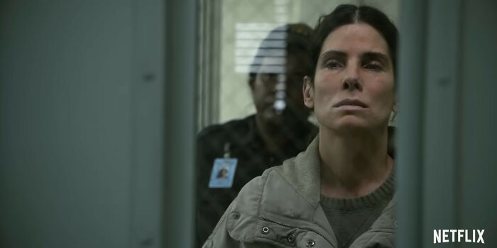 Woman in a gray jacket with serious expression behind a glass door in a scene from Netflix movies that disappointed viewers.