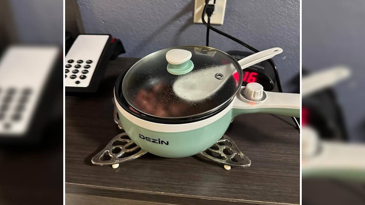 Compact electric cooking pot with glass lid on a dorm desk, a genius dorm find for surviving freshman year.