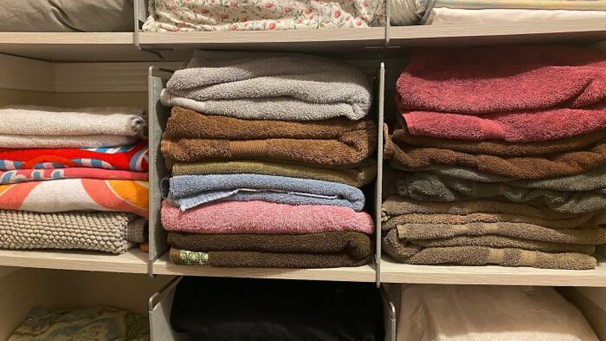 Closet shelf dividers organizing folded towels and blankets to maximize space in a chaotic home corner.