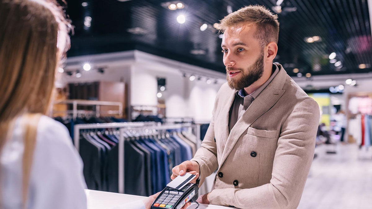 Man using credit card at store counter, engaging in smooth pickup lines conversation with cashier.