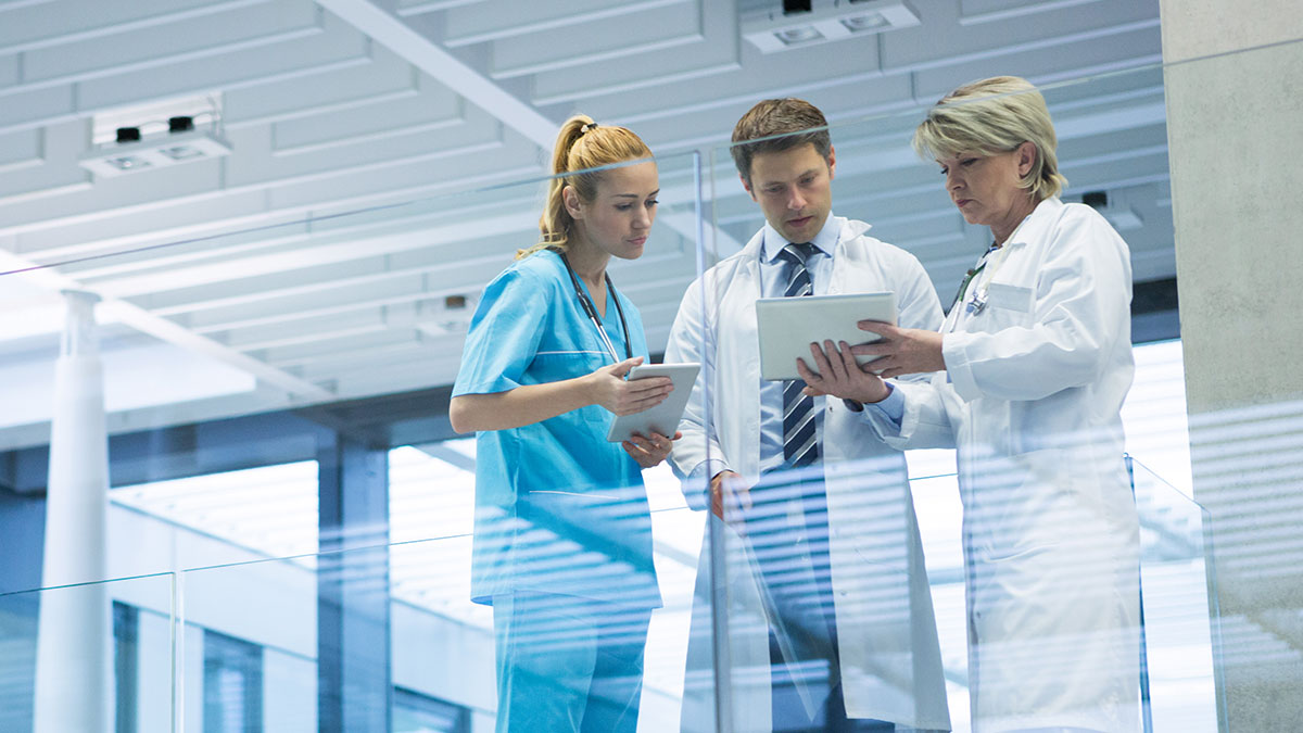 Three medical professionals discussing patient data on tablets in a modern hospital setting with reverse culture shock concept.