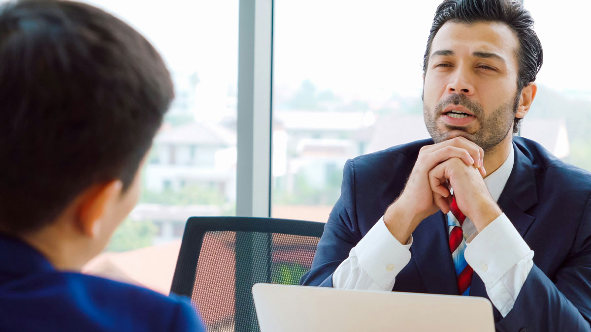 Man in a business suit discussing work knowledge before PTO during a meeting with a colleague in an office setting.
