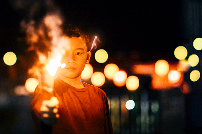 Boy holding a sparkler at night with glowing lights in the background, illustrating grieving son and family conflict. Boy holding a sparkler at night with glowing lights in the background, illustrating grieving son and family conflict.