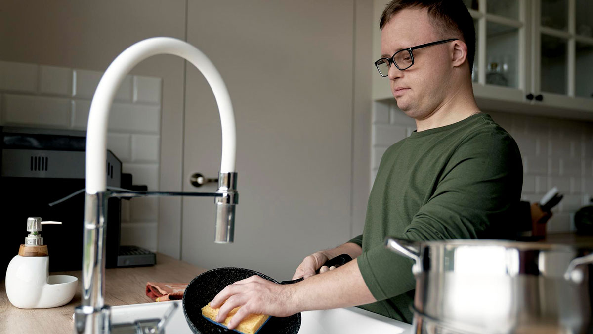 Man washing dishes in kitchen, illustrating chores and roomie treated like help by boss-like boyfriend behavior.