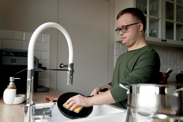 Man washing a pan in the kitchen sink, highlighting chores and treatment of kind roomie by boyfriend.