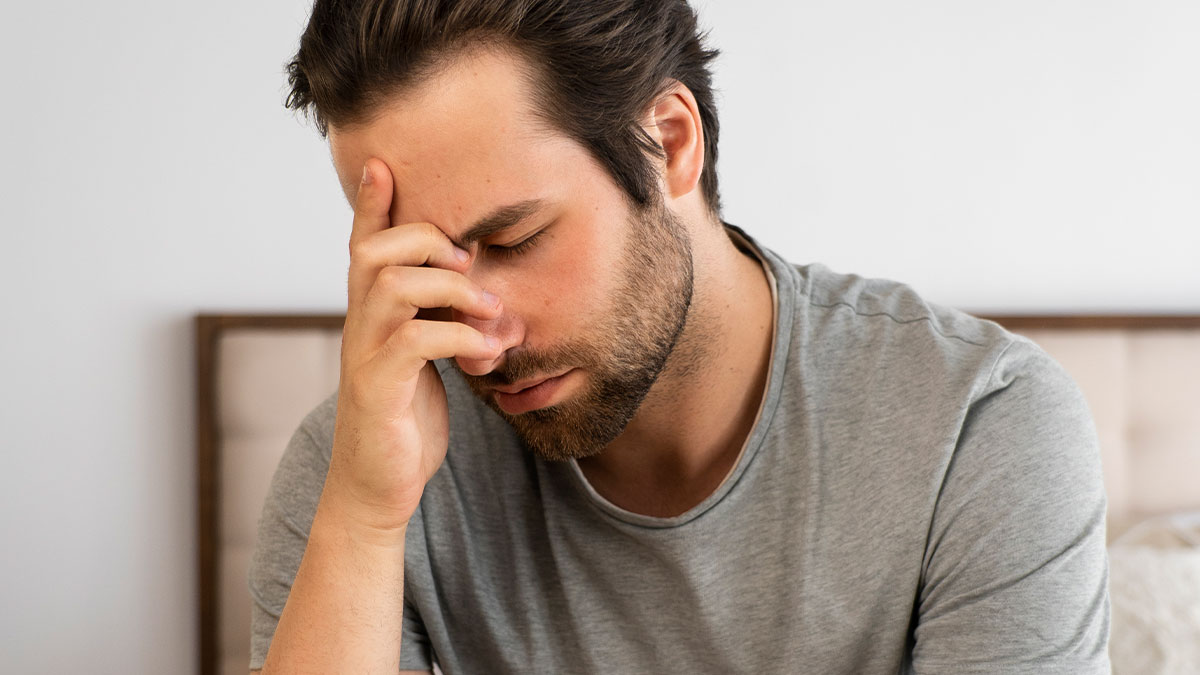 Man sitting stressed in a bedroom, showing frustration after giving pregnant girlfriend an ultimatum over insecurities.