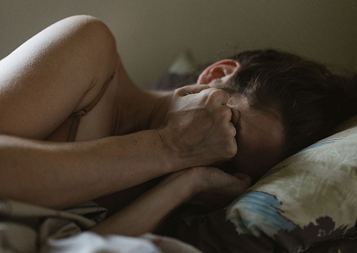 Woman lying in bed covering face, experiencing heartbreak and emotional pain after mother’s death reveals boyfriend’s true character.