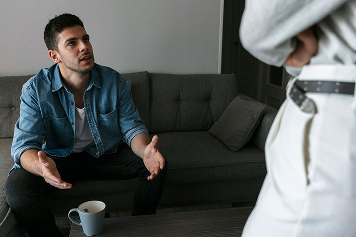 Man pretending to be single makes excuses while having a tense conversation with girlfriend in a living room setting. Man pretending to be single makes excuses while having a tense conversation with girlfriend in a living room setting.