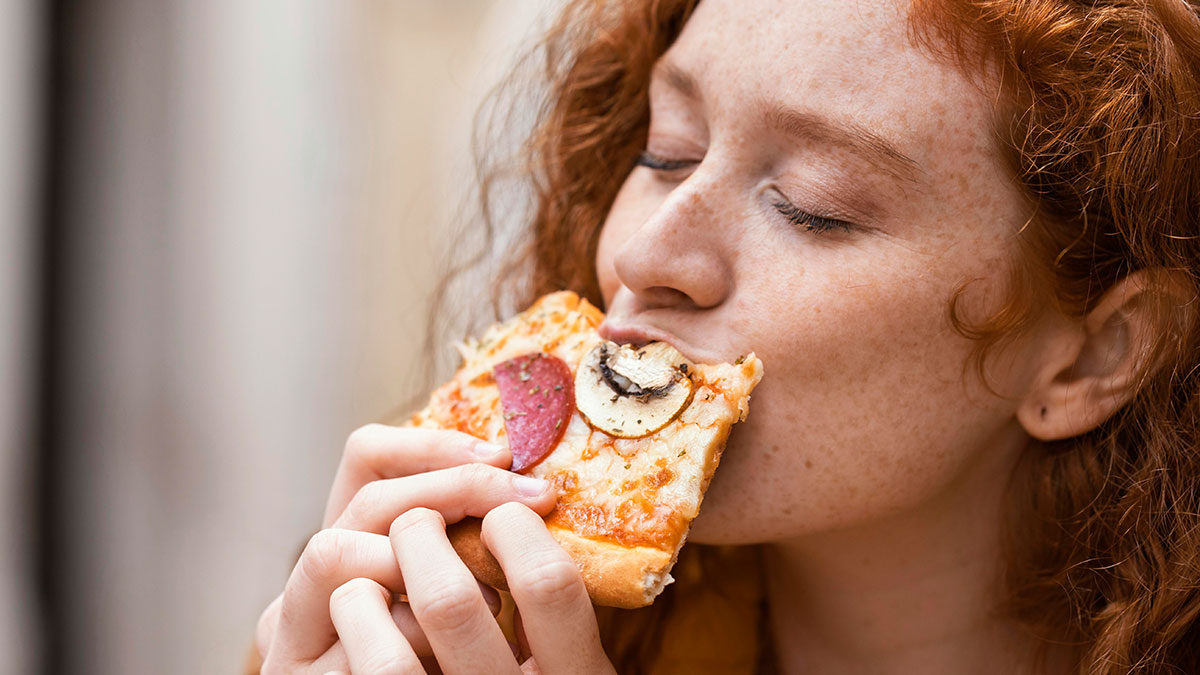 Worker enjoying a slice of pizza with pepperoni and mushrooms, highlighting a gluten-free colleague at a pizza party.