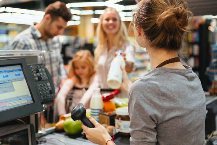 Cashier scanning groceries at checkout while family waits, illustrating picking the wrong line at the grocery store scenario.