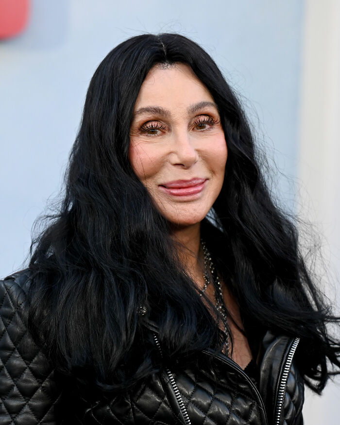 Cher with long black hair and a black quilted jacket, highlighting her melting appearance and plastic surgery concerns. Cher with long black hair and a black quilted jacket, highlighting her melting appearance and plastic surgery concerns.