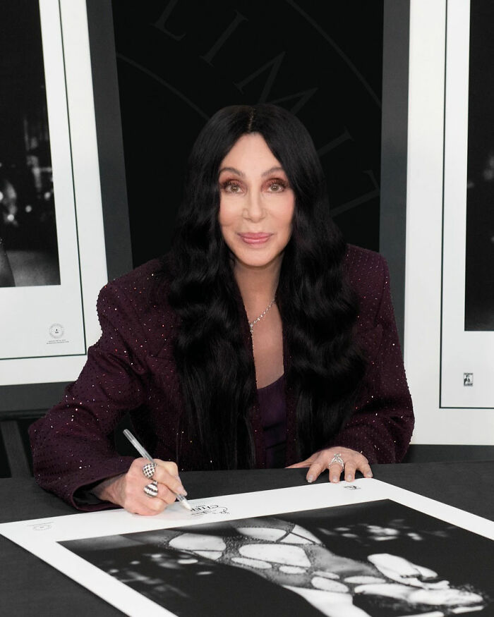 Cher signing a photograph at an event, highlighting concern over her melting appearance and plastic surgery indulgence. Cher signing a photograph at an event, highlighting concern over her melting appearance and plastic surgery indulgence.