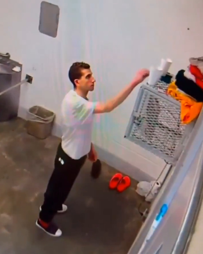 Bryan Kohberger inside jail cell with red hands, reaching for items while standing near a metal storage rack. Bryan Kohberger inside jail cell with red hands, reaching for items while standing near a metal storage rack.