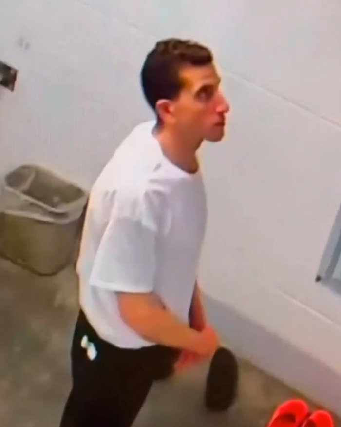 Bryan Kohberger in jail wearing white shirt with red hands standing near cell wall and belongings in a sparse prison setting Bryan Kohberger in jail wearing white shirt with red hands standing near cell wall and belongings in a sparse prison setting