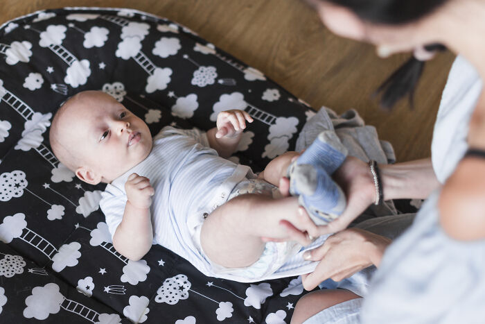 Adult changing a baby's diaper on a black and white patterned mat, illustrating gender-based double standards in caregiving roles.