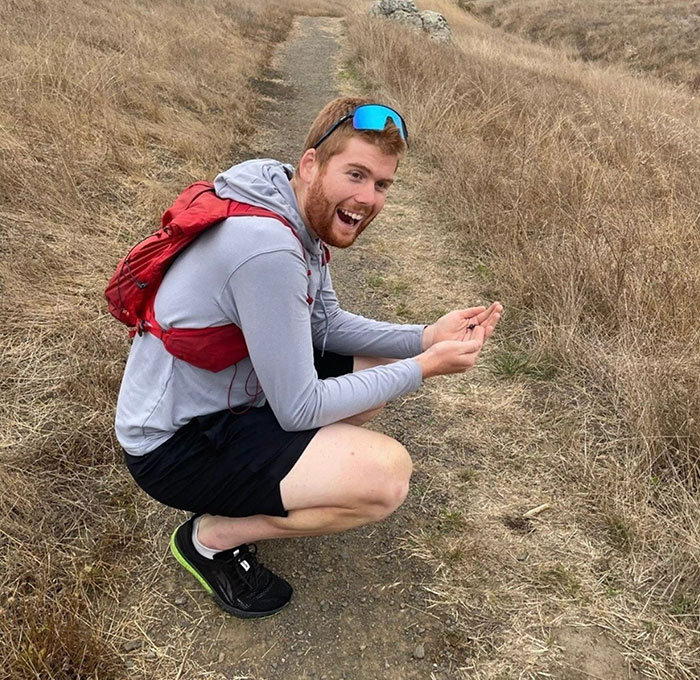 Smiling man with a red backpack crouching on a dirt path surrounded by dry grass, representing a Good Samaritan outdoors. Smiling man with a red backpack crouching on a dirt path surrounded by dry grass, representing a Good Samaritan outdoors.
