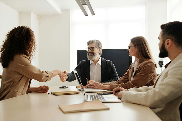 Woman sitting back at office meeting table, watching colleague who stole her job shake hands with a man. Woman sitting back at office meeting table, watching colleague who stole her job shake hands with a man.
