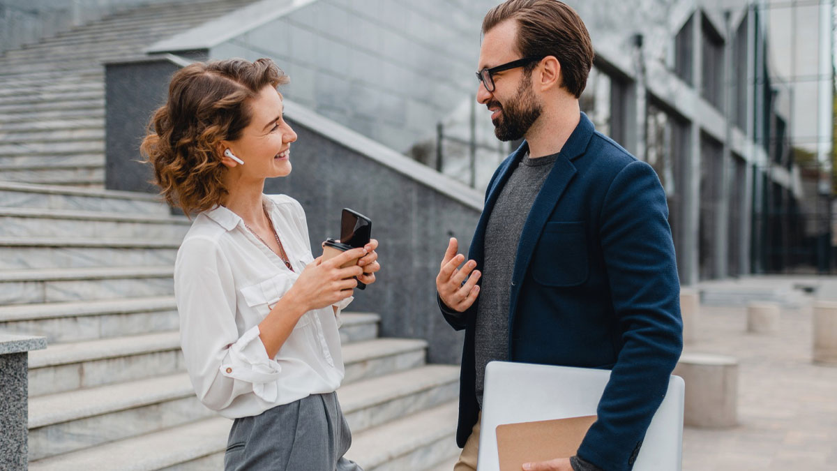 Colleague trouble at work as man and woman smile and chat outside office building near stairs.