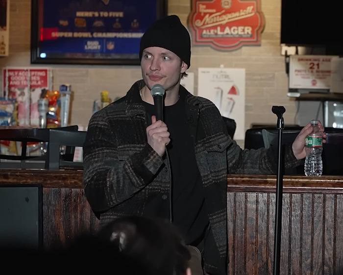 Comedian Matt Rife performing stand-up comedy indoors, wearing a beanie and holding a microphone and water bottle. Comedian Matt Rife performing stand-up comedy indoors, wearing a beanie and holding a microphone and water bottle.