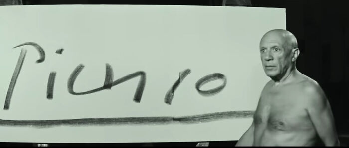 A shirtless man stands beside a board with handwritten text, illustrating concept time facts visually in a dark setting.