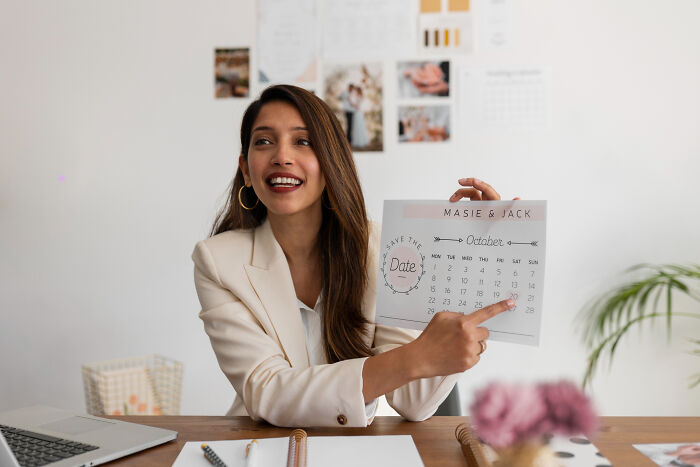 Woman in a beige blazer holding and pointing at a calendar, illustrating concept time facts in a bright office setting.