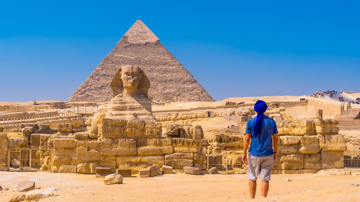 Tourist in blue clothes viewing the Great Sphinx and Pyramid of Giza under clear sky with concept time facts theme.