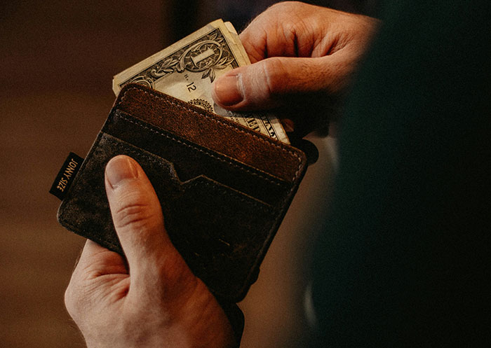 Person holding a wallet and placing a dollar bill inside, illustrating the ups and downs of going from rags to riches.