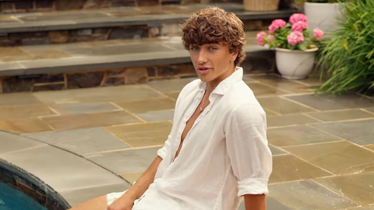 Young man with curly hair by poolside in casual white shirt, an ad highlighting genetics sparks woke outrage online.