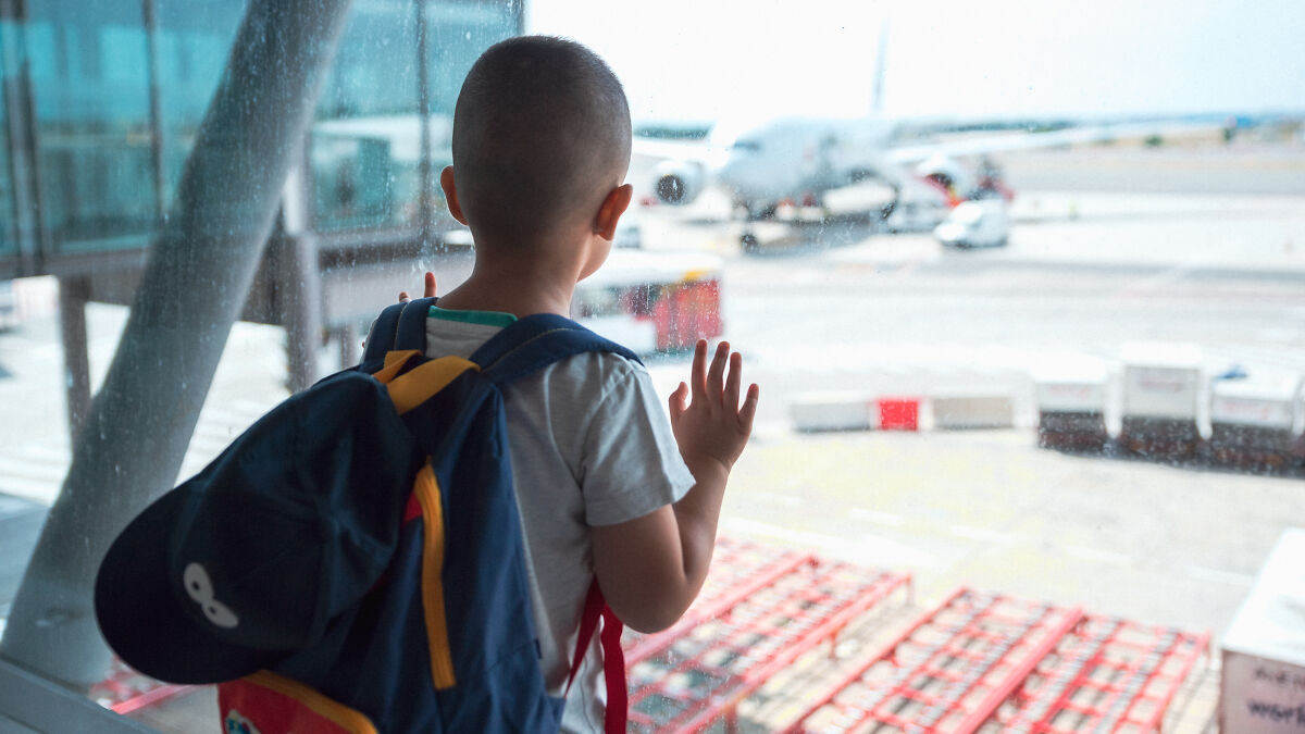 Young boy with backpack looking out airport window at airplane, highlighting parents abandoning son at Barcelona airport case.