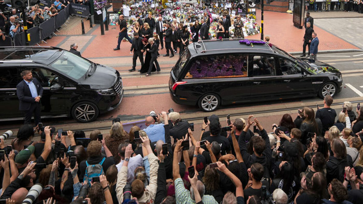 Crowd gathers at funeral procession with hearse, related to lawyers explaining buying Ozzy Osbourneu2019s house with grave backyard
