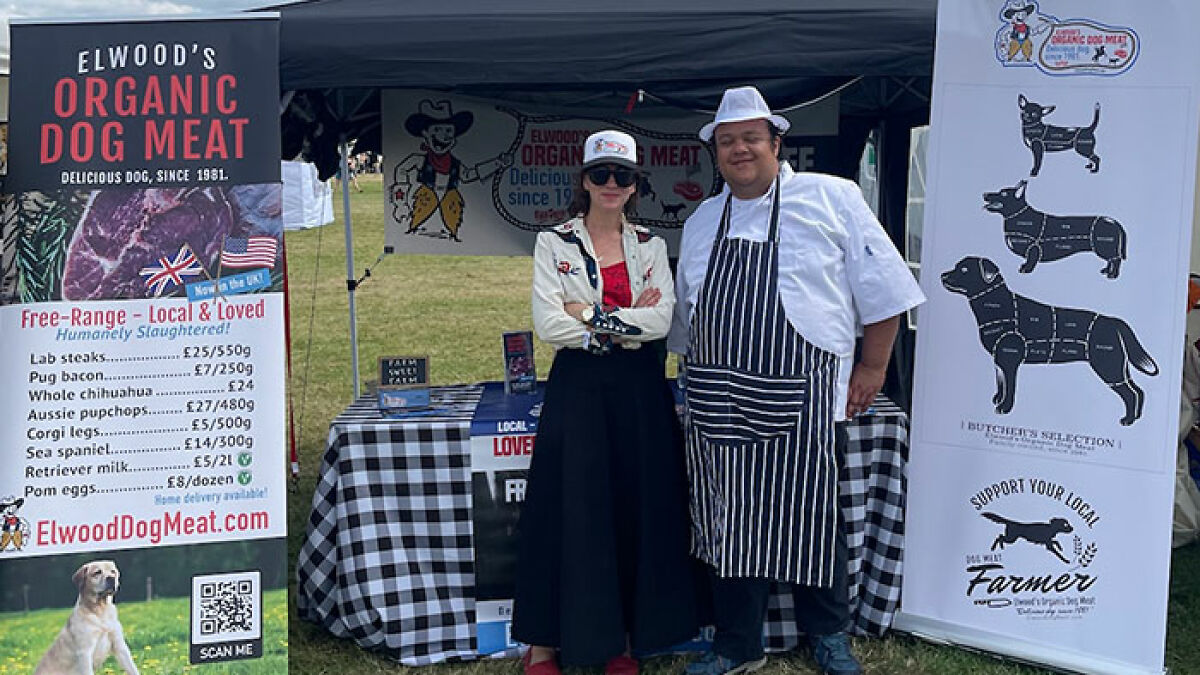 Owner of dog meat farm standing by a stall with signs promoting organic dog meat and local farm support.