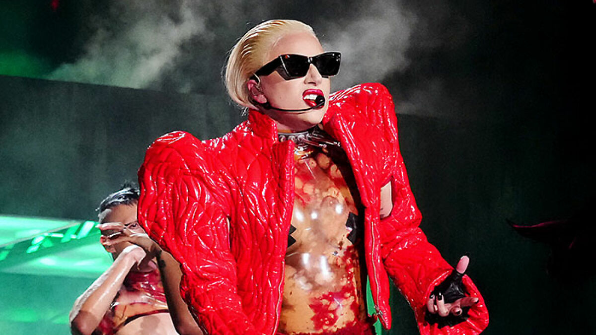 Lady Gaga performing on stage in a red jacket and sunglasses amid backlash for ageist and misogynistic comments.