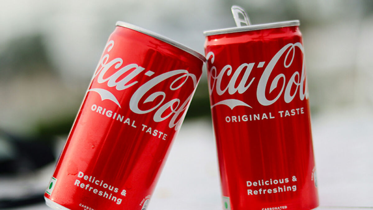 Two red Coca-Cola cans with original taste label, highlighting cane sugar swap and consumer health concerns.