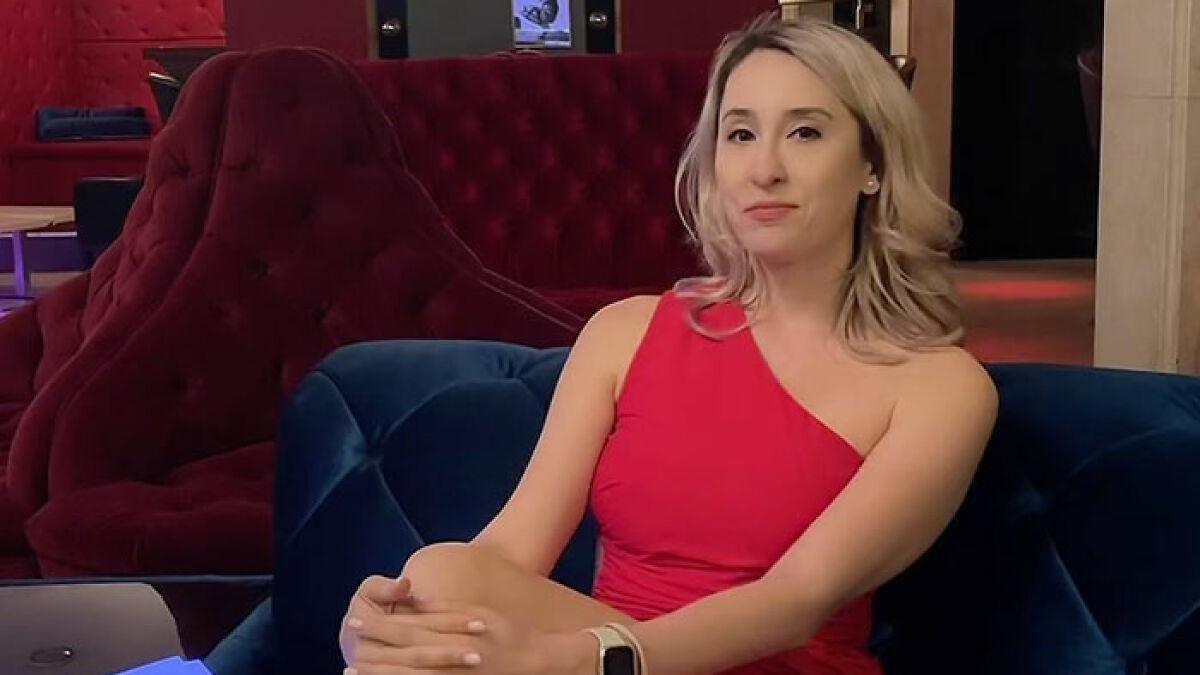Brothel manager in a red dress seated on a blue couch, discussing the most stupid ways men get caught by partners.