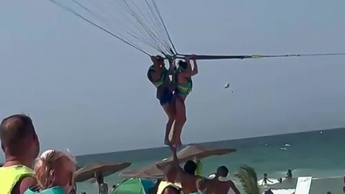 Two people parasailing mid-air over the ocean, highlighting a mid-air a*****t incident during the activity.