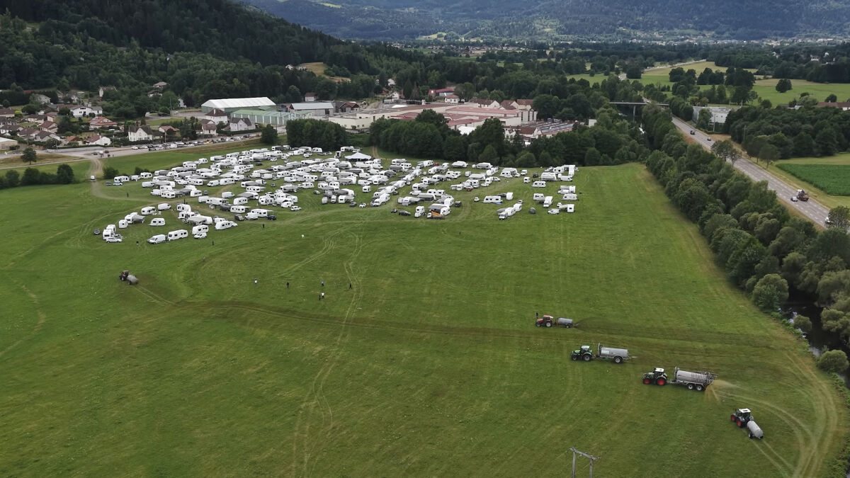Wide aerial view of a field with caravans and farmers spraying manure on squatters in a rural landscape.