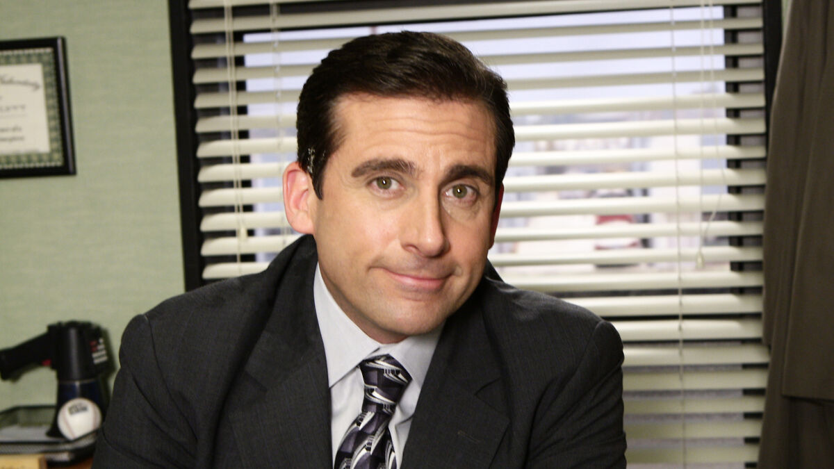 Actor portraying Michael Scott from The Office cast sitting in an office setting with blinds in the background