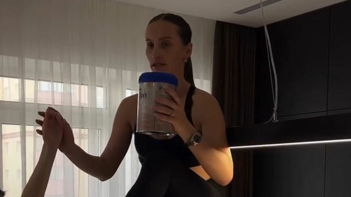 Influencer recovering from spine injury after falling during Nicki Minaj stiletto challenge, sitting indoors holding a container.