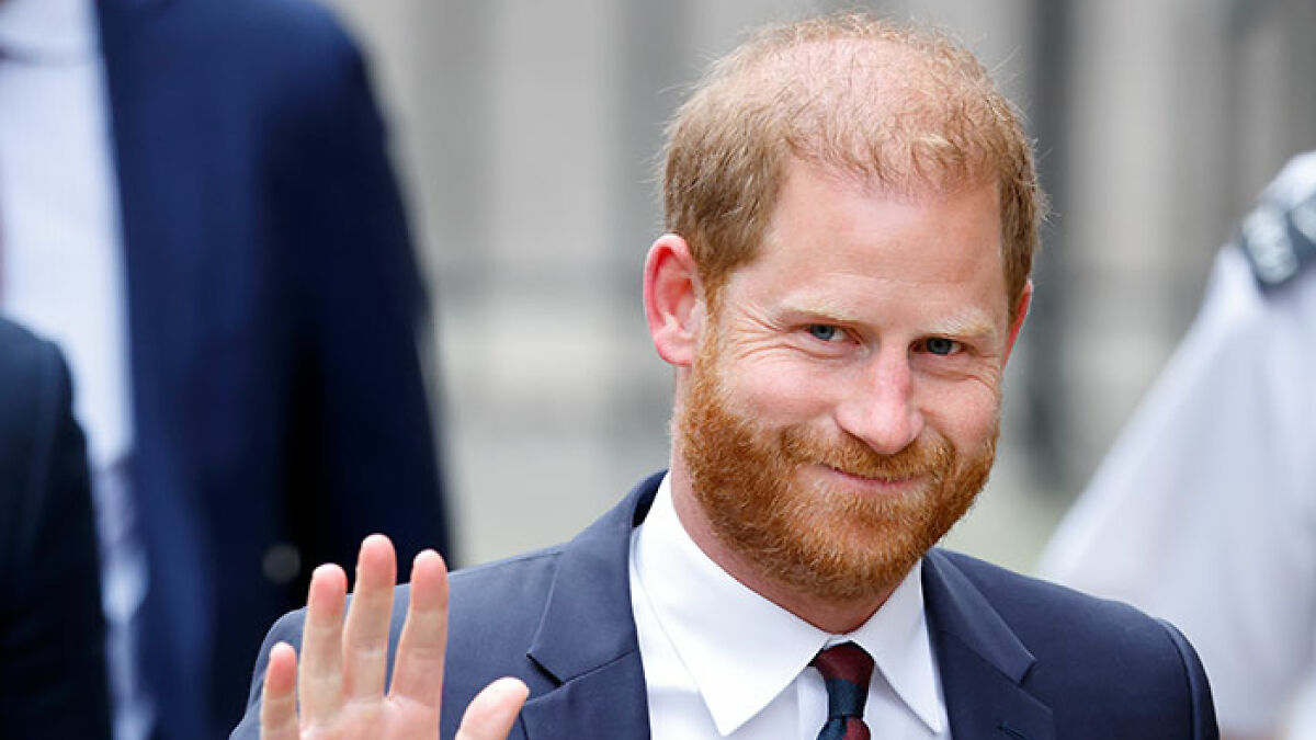 Prince Harry waving outdoors, wearing a suit and tie, responding after Sentebale scandal investigation findings are public.