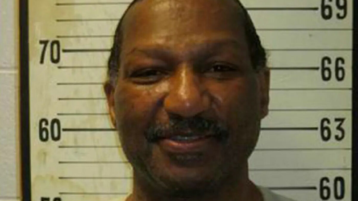 Mugshot of inmate with height chart background related to inmate cries during painful e*******n and defibrillator refusal.